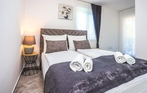 Ein ordentlich bezogenes Bett mit dunklem Kopfteil, weißen Kissen und einem zusammengerollten Handtuch.