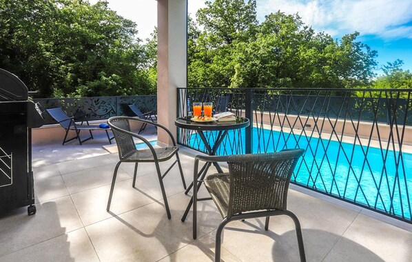 Ein Balkon mit Pool, zwei Korbstühle, einem Tisch mit Getränken und einem Grill.