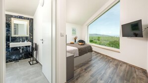 A modern bathroom with a marble sink and a shower, a bedroom with a large window and a bed, and a TV mounted on the wall. - Stunning home in Krnica (Krnica)