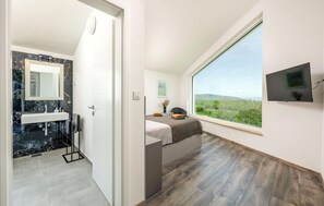 A modern bathroom with a marble sink and a shower, a bedroom with a large window and a bed, and a TV mounted on the wall. - Stunning home in Krnica (Krnica)