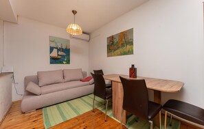 Ein kleines Zimmer mit einer Couch, einem Esstisch, Stühlen, einer Pendelleuchte und zwei Bildern an den Wänden.