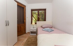 Ein Schlafzimmer mit Bett, Nachttisch, Fenster mit Blick auf Bäume und einer Tür.