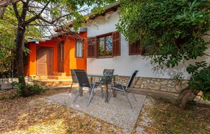 Eine Terrasse mit Tisch und Stühlen, eine Steinmauer und ein Gebäude mit orangefarbenen und weißen Wänden sowie Holzjalousien.