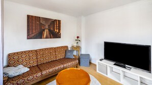 Un soggiorno con un divano a fantasia, una televisione a schermo piatto, una lampada decorativa a soffitto e un quadro appeso al muro.