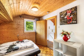 Una habitación con paneles de madera, una cama, un ventanal, una puerta y un cuadro colgado en la pared.