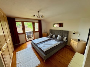 A bedroom with a large bed, a ceiling fan, a window with curtains, a bedside table, and a nightstand.