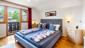 Una camera da letto con un letto matrimoniale, un comodino, una cassettiera, uno specchio e un balcone che si affaccia su alberi.