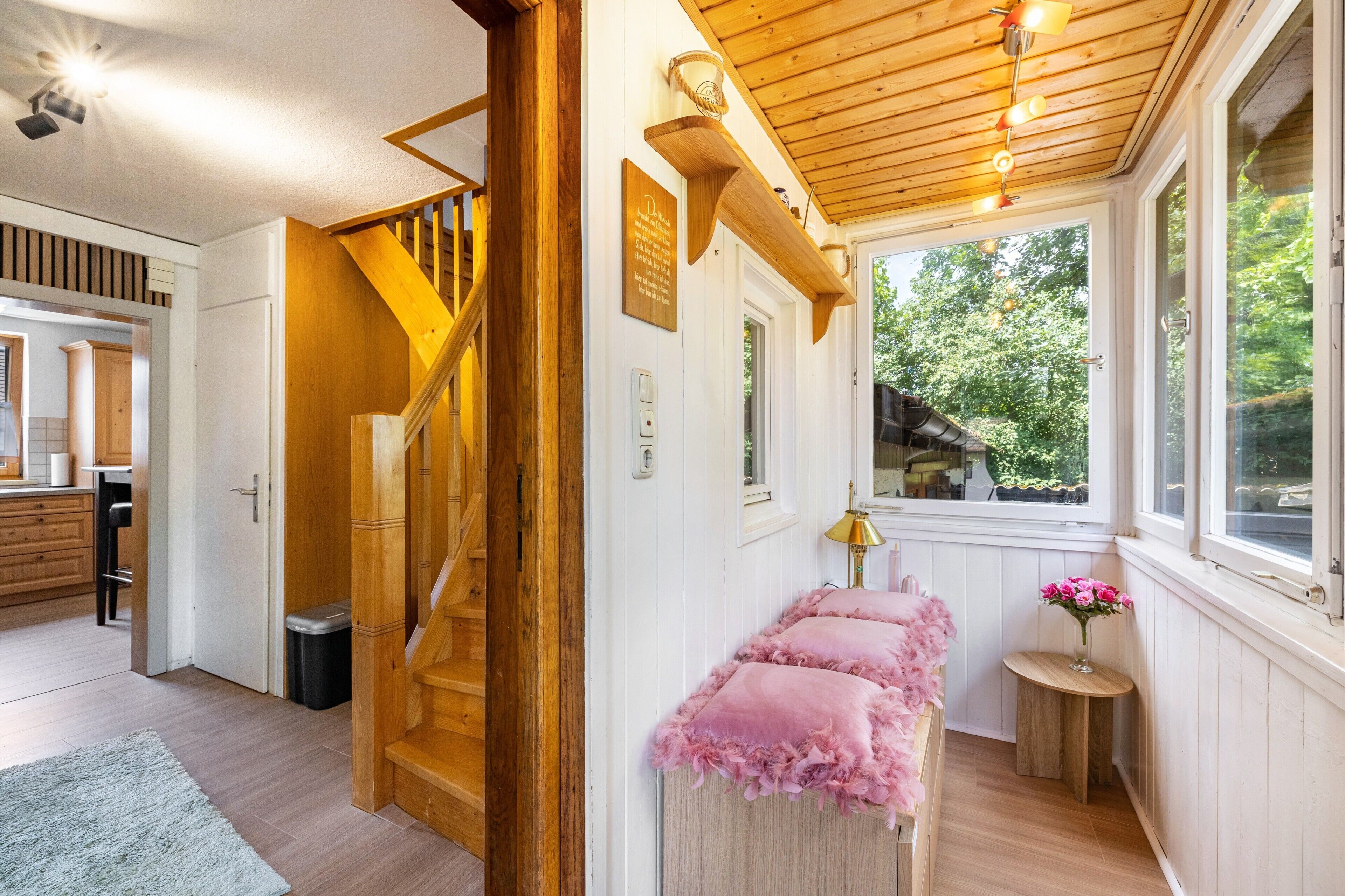 Una scala in legno conduce al secondo piano, con una piccola panca con cuscini rosa e una finestra che si affaccia sul verde.