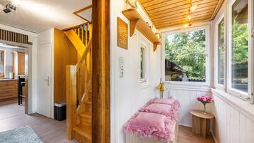 Una scala in legno conduce al secondo piano, con una piccola panca con cuscini rosa e una finestra che si affaccia sul verde.