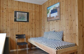 Une pièce aux murs en bois, un lit avec une literie à motifs, une chaise et deux œuvres d’art encadrées.
