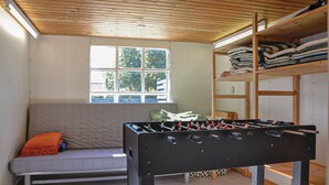 A room with a sofa, a foosball table, a window, and a shelving unit with folded blankets.