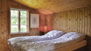 A wooden-paneled room with a bed, a window, and a nightstand with a lamp.
