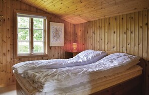Een kamer met houten lambrisering, een bed, een raam en een nachtkastje met een lamp.