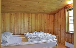 Un lit simple dans une pièce aux murs en bois et dotée d’une fenêtre.
