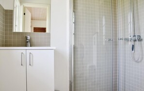 Een badkamer met een douche, een wastafel met spiegel en kastjes.