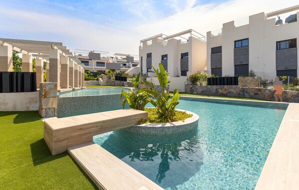 Ein moderner Poolbereich mit klarem Pool, einer kleinen Wasserfallanlage und einer Steinwand mit Pflanzen.