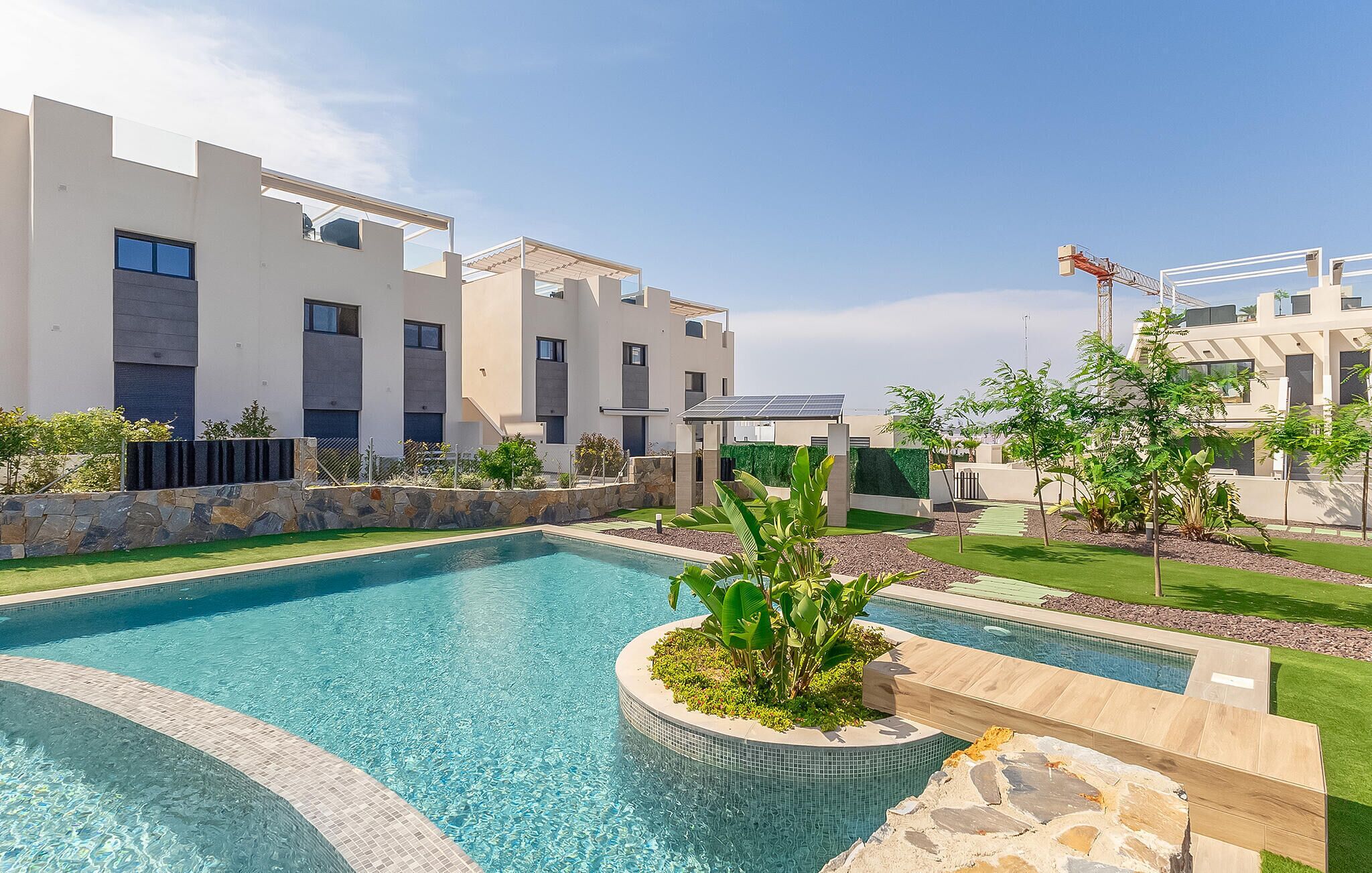 A modern residential complex with a swimming pool, stone walls, and greenery.