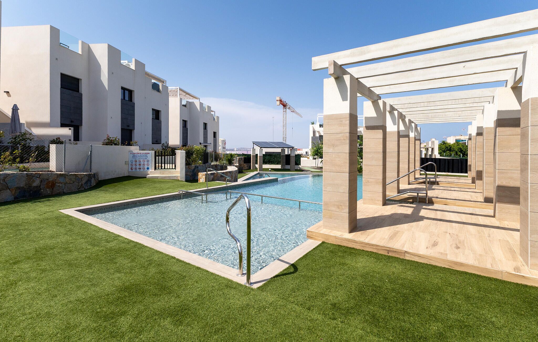 Une piscine dotée d’une pergola, d’un espace clos et offrant une vue sur une grue de chantier en arrière-plan.
