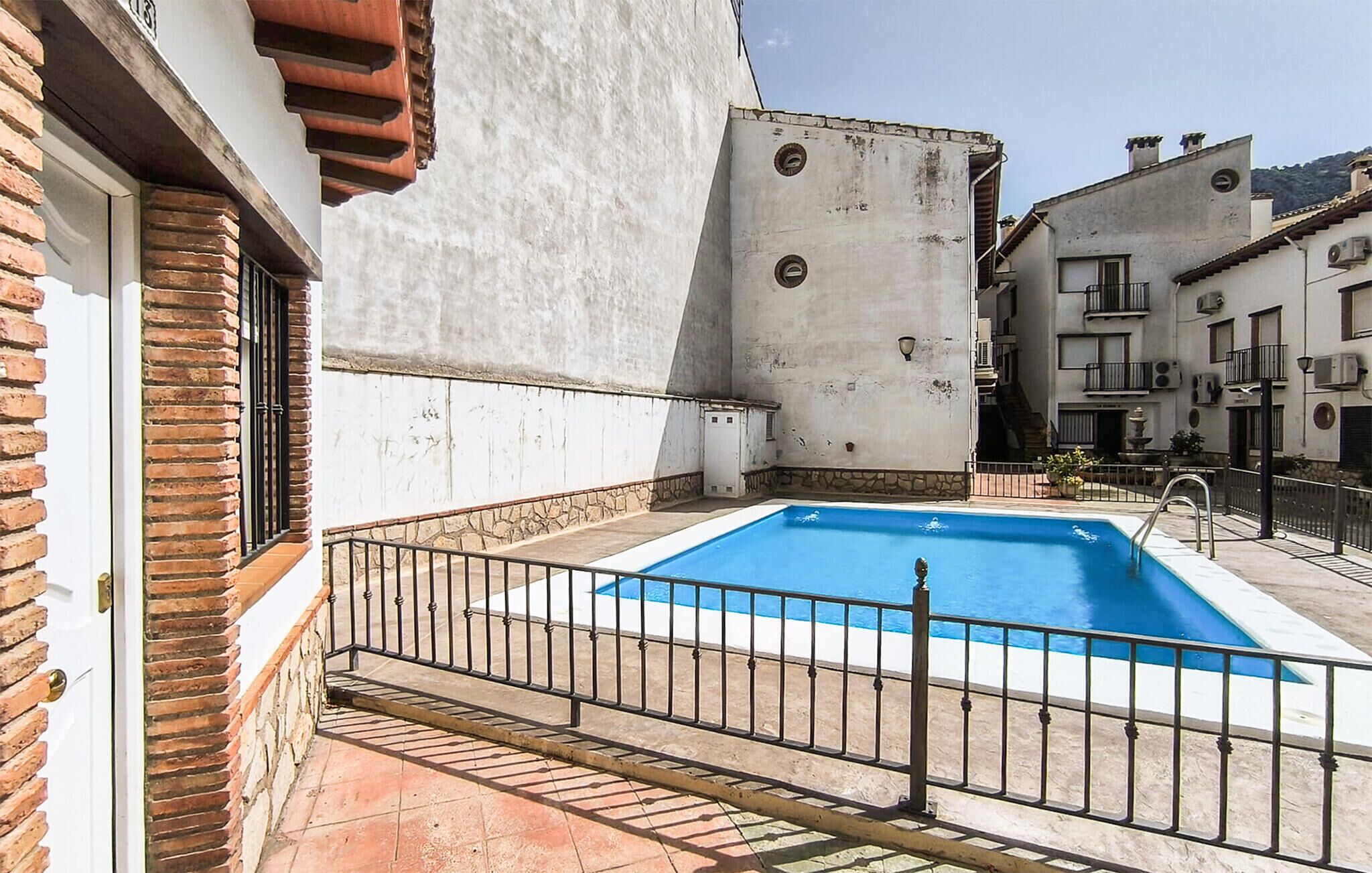 Una piscina con una cerca de metal, un muro de ladrillo y un edificio blanco con balcón.