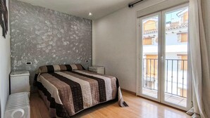 Ein Schlafzimmer mit Bett, Heizkörper, Fenster mit Blick auf ein Gebäude und einem Balkon.