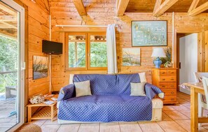 Ein Holzblockhaus-Interieur mit einem blau gesteppten Sofa, einem Fernseher und Bildern an den Wänden.