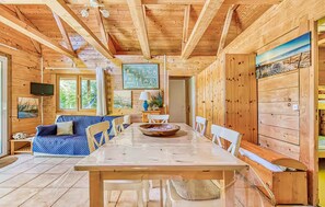 Ein Holzblockhaus-Innenraum mit Esstisch, Stühlen, einer Couch und einem an der Wand befestigten Fernseher.