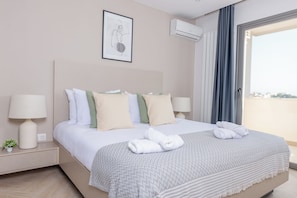A hotel room with a bed, two bedside lamps, a small plant, a framed artwork, and an air conditioning unit.