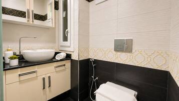 A modern bathroom with a white sink, black countertop, beige cabinets, a black shower enclosure, and patterned wall tiles.