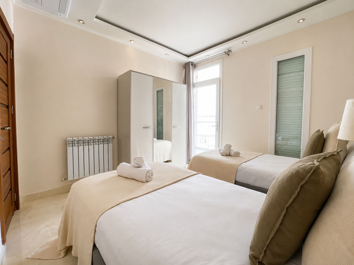 Habitación de hotel con dos camas, un radiador, un espejo grande y una ventana con persianas.
