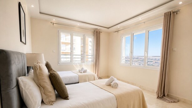 Ein modernes Hotelzimmer mit einem großen Bett, zwei Einzelbetten, einem Sofa und Blick auf die Stadt.