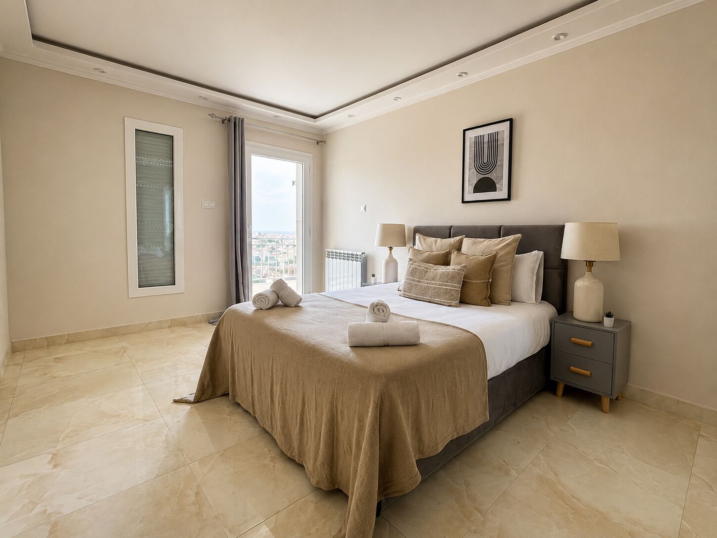 Habitación de hotel con cama, mesitas de noche, vista por la ventana y un cuadro en la pared.