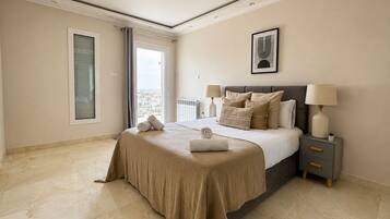 Habitación de hotel con cama, mesitas de noche, vista por la ventana y un cuadro en la pared.