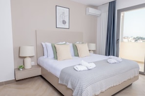 A hotel room with a bed, two bedside tables with lamps, a small plant, a framed artwork, and a view through a window.