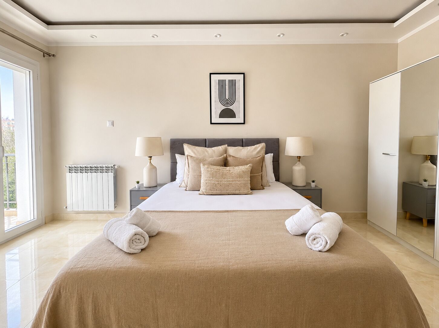 A bedroom with a large bed, two bedside tables with lamps, a radiator, and a framed artwork on the wall.