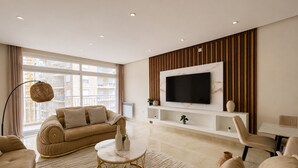 Ein modernes Wohnzimmer mit einer Couch, einem Couchtisch, einem an der Wand montierten Fernseher und einem Fenster mit Vorhängen.