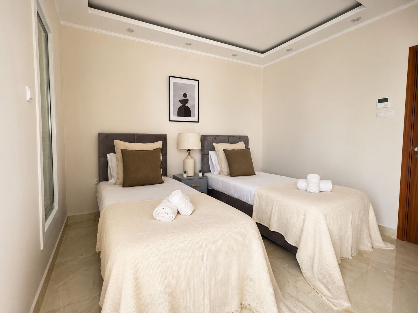 Habitació d'hotel amb dos llits, una taula de nit amb una làmpada, un quadre encadrejat a la paret i una porta de fusta.