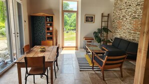 A room with a wooden table, chairs, a sofa, a bookshelf, and a stone wall. - Tastefully renovated 18th century farmhouse, landscaped gardens and access to the château grounds (Treillières)