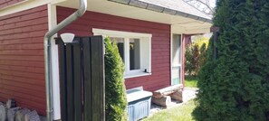 Une maison rouge avec une terrasse en bois, une fenêtre et un petit abri de jardin.