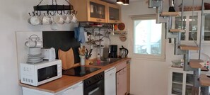 Une cuisine compacte équipée d’un four à micro-ondes, d’un grille-pain et d’une machine à café, avec des meubles en bois et un porte-ustensiles suspendu.