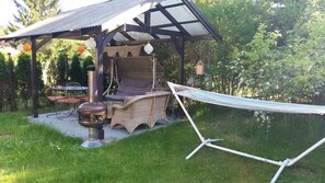 Un espace extérieur aménagé, abrité, avec un barbecue, un hamac et une table avec des chaises.