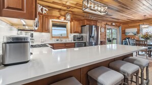 Una cocina con gabinetes de madera, un refrigerador de acero inoxidable, una isla grande con taburetes y una lámpara colgante.