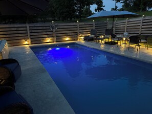 En swimmingpool med træterrasse, liggestole og et hegn.