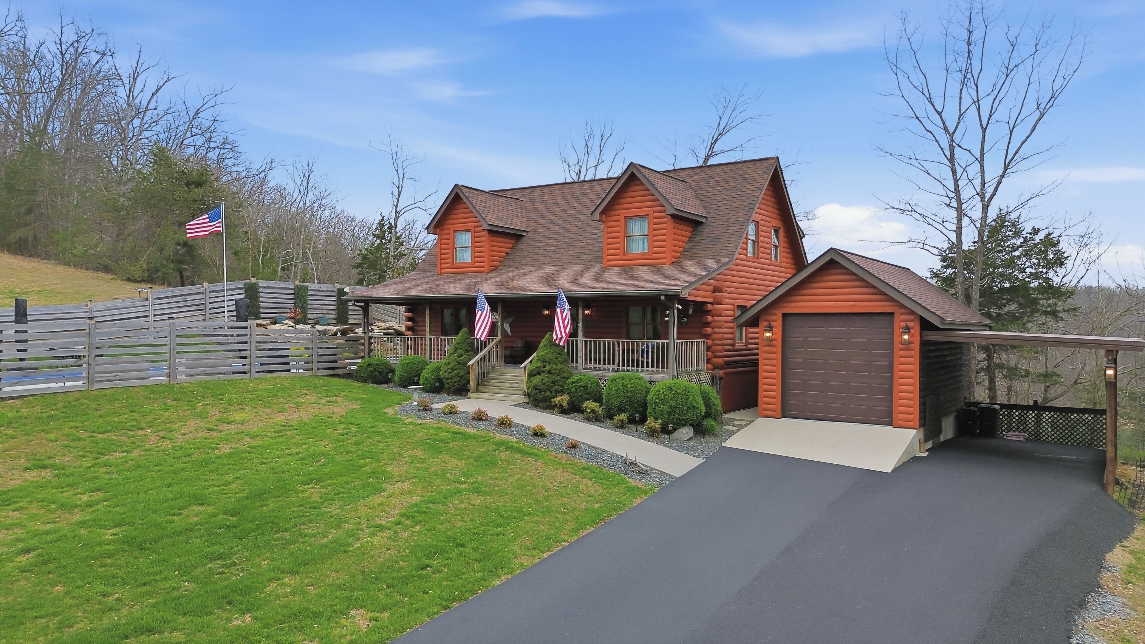 A two-story log cabin with a porch, a garage, and a driveway.