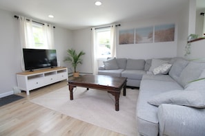 A living room with a flat-screen TV, a sofa, a coffee table, and a potted plant. - Newly Renovated Marshview Retreat in the Heart of Wellfleet (2440) (Wellfleet)