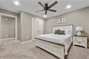 A bedroom with a bed, a nightstand, a lamp, a ceiling fan, and a door. - 3 Bedroom Duplex - The Gardens Cottage Duo A (Houston)
