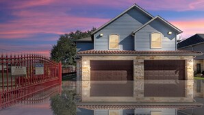 Une maison à deux étages avec un garage, un portail rouge et son reflet net dans l’eau.