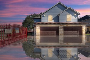 A two-story house with a garage, a red gate, and a clear reflection in the water. - 3 Bedroom Duplex - The Gardens Cottage Duo A (Houston)