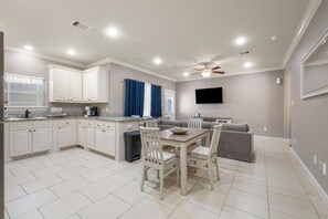 A modern kitchen with white cabinets, a dining table with chairs, a gray sofa, and a ceiling fan. - 3 Bedroom Duplex - The Gardens Cottage Duo A (Houston)