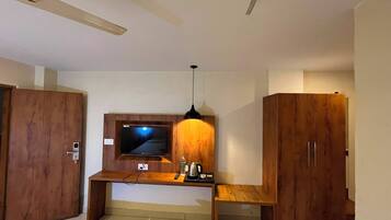 A room with a wooden desk, a television, a pendant light, and wooden wardrobes.