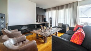 Ein modernes Wohnzimmer mit Kamin, schwarzen und braunen Ledersofas, einem Holztisch und einem großen Fenster mit Vorhängen.